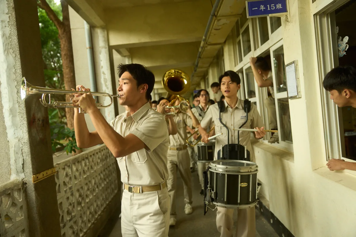 校舎の廊下で演奏しながら行進する男子高校生たち。映画『進行曲 マーチングボーイズ』場面写真